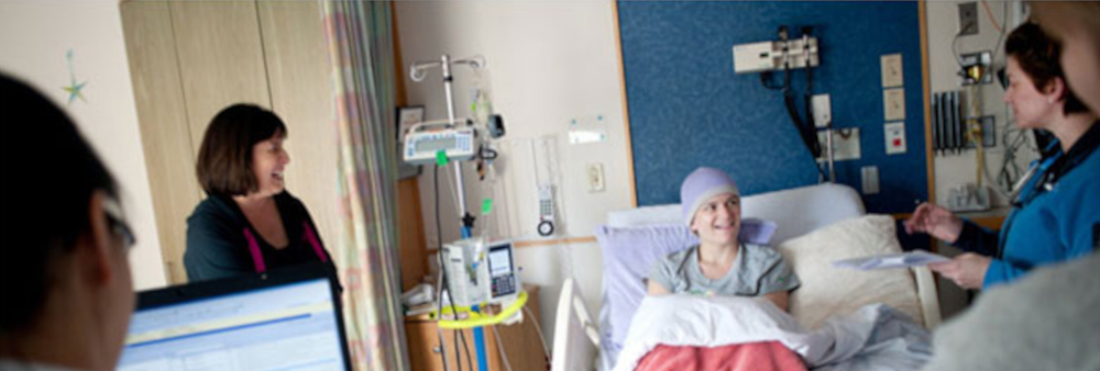 Clinicians speak with patient laying in bed; woman stands to patient's right