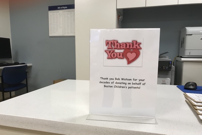 Sign on check-in desk reads: "Thank you," with heart graphic, followed by "Thank you Bob Watson for your decades of donating on behalf of Boston Children's patients!"