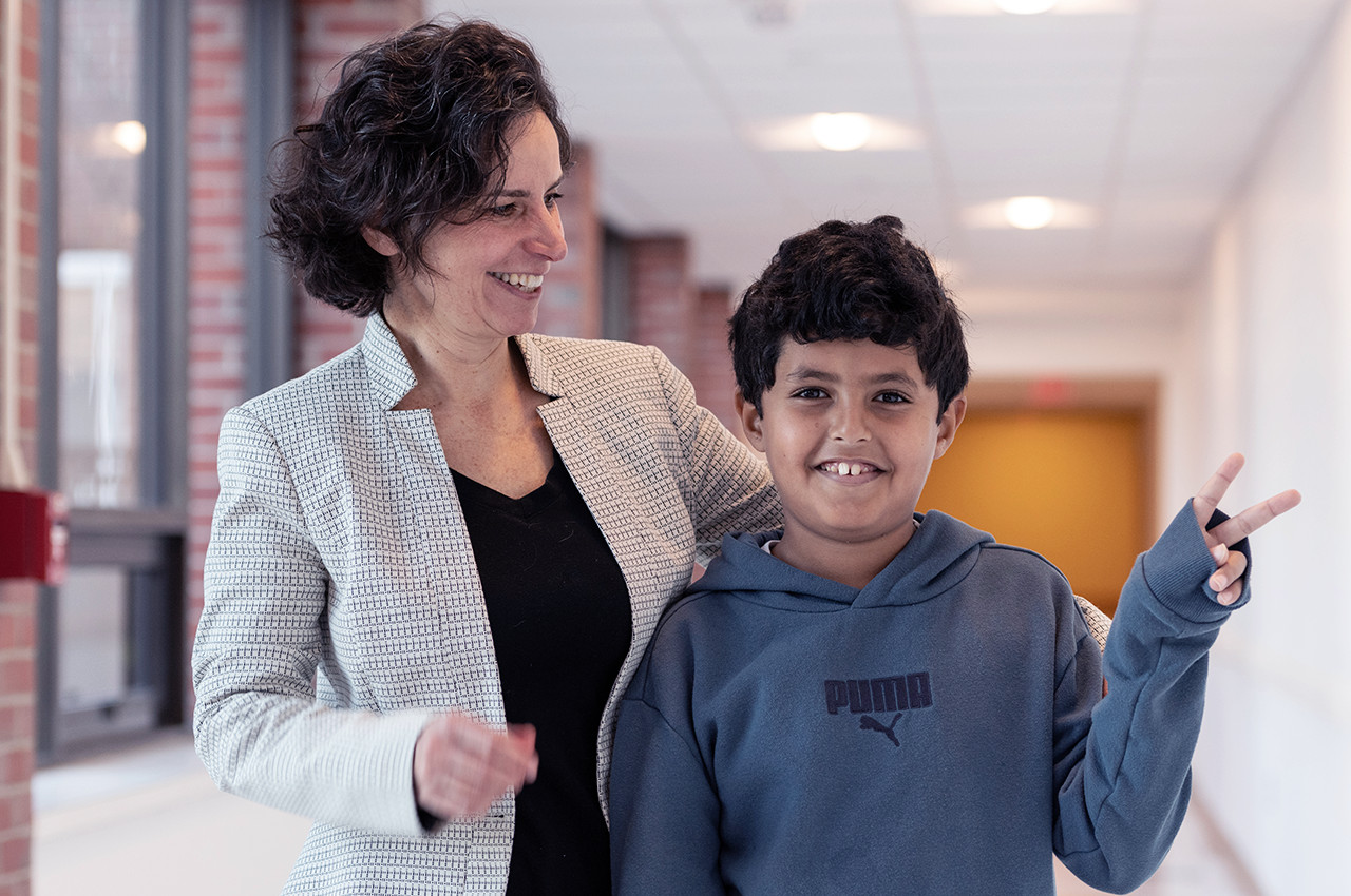 a boy holding up a peace sign as his mother looks on