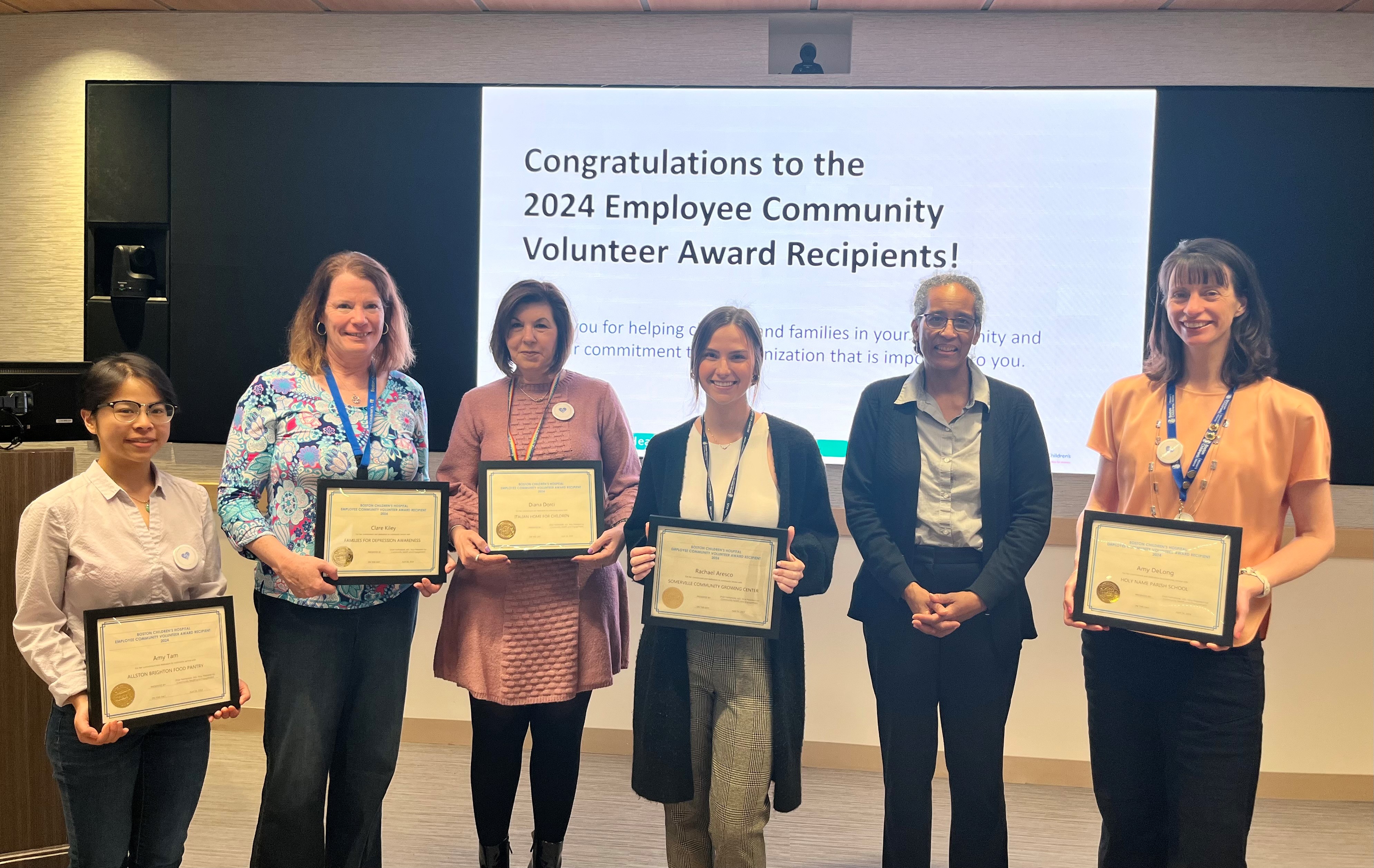 Women stand in front of projector, holding awards certificates