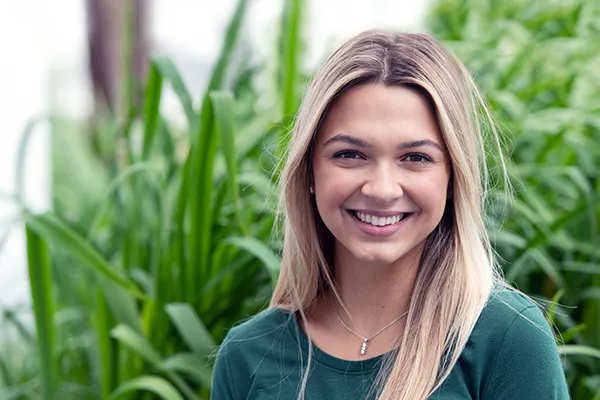 Teenage girl standing in front of garden smiles for camera
