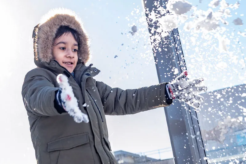 A boy in a green parka throws a handful of snow out in front of him.