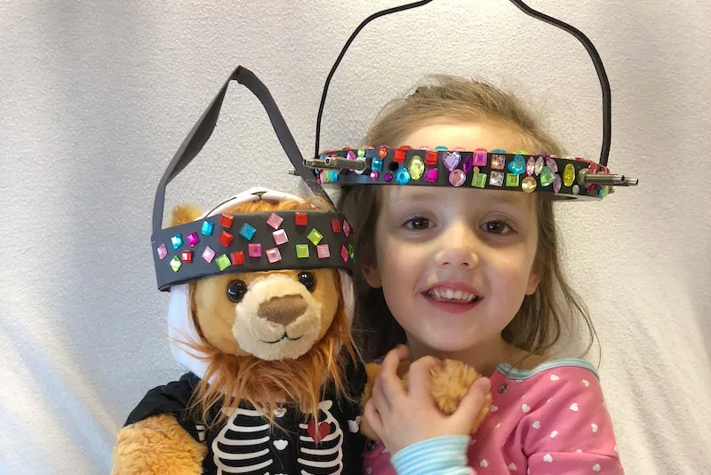 Gracie holds a teddy bear also wearing a halo like she is.