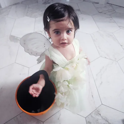 Toddler girl wearing angel outfit stares up at camera