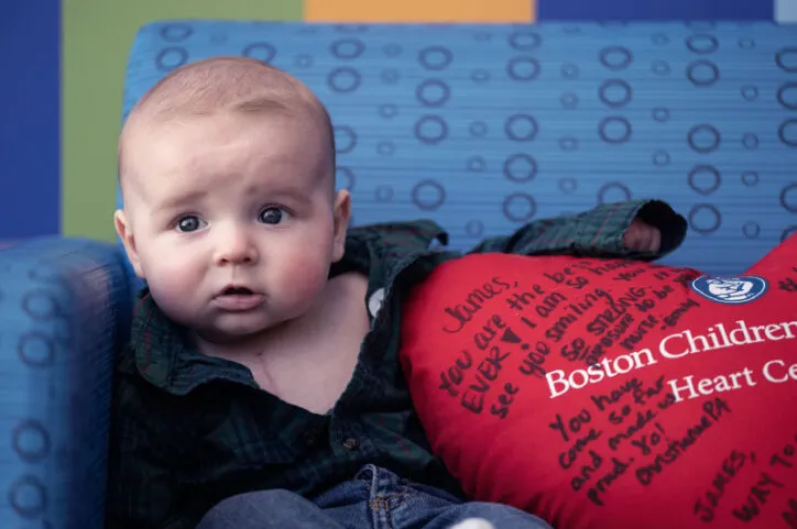 Young boy swaddled in fleece is surrounded by stuffed heart signed by care team at Boston Children's