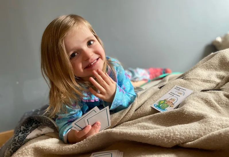Smiling young girl lay on blanket while holding game cards in her right hand