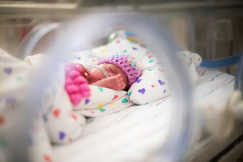 Baby wearing hat sleeps in bed in nursery shortly after birth