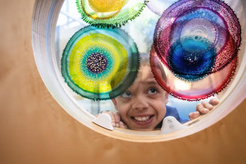 Young boy looks through door window that has splotches of color