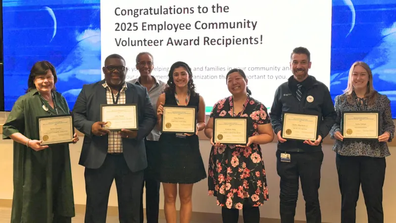 Women and men stand in front of projector, holding awards certificates