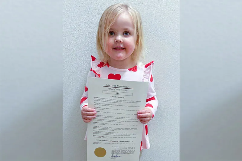 Blittle blonde haired girl holds official document in front of camera