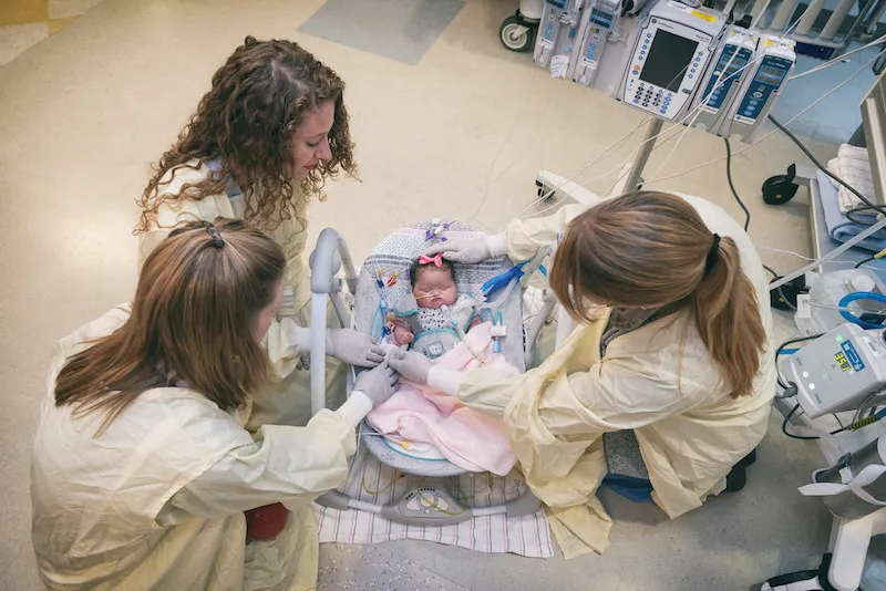 Three clinicians look over baby in seat on floor