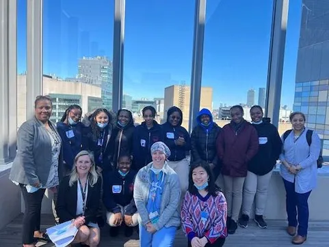 eleven teenagers and three women on a rooftop in front of a city skyline