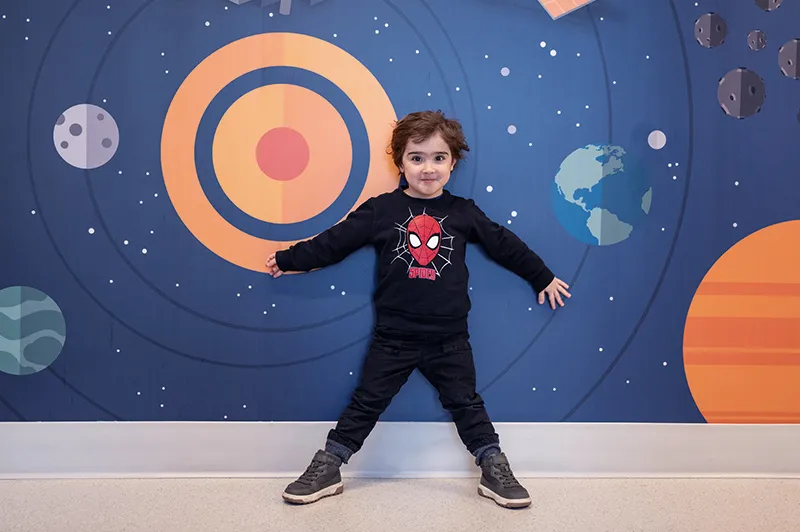 Boy in black outfit stands against a colorfully painted wall with spheres against a blue background