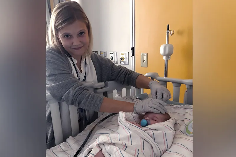 Clinician swaddles baby in blanket as baby lay on hospital bed