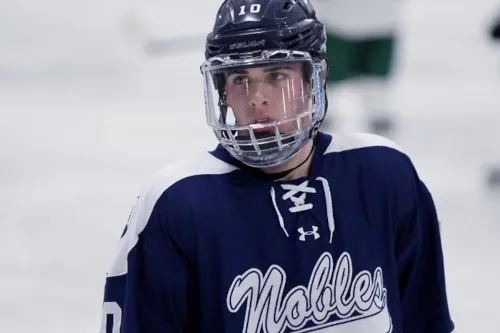 Teen hockey player wearing helmet and visor skates on rink