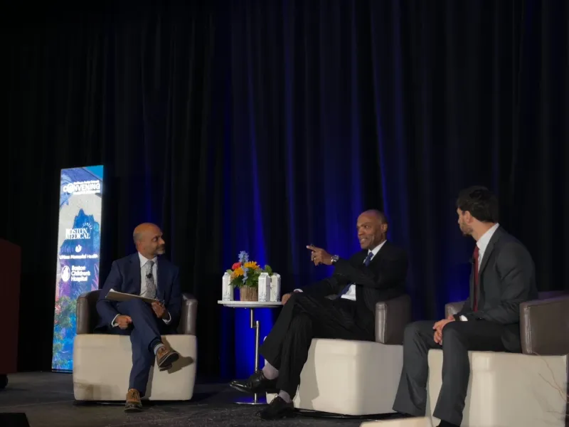 Three men sit on stage and speak with audience during presentation